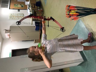 A young girl holds a bow as she follows the steps to archery success. 
