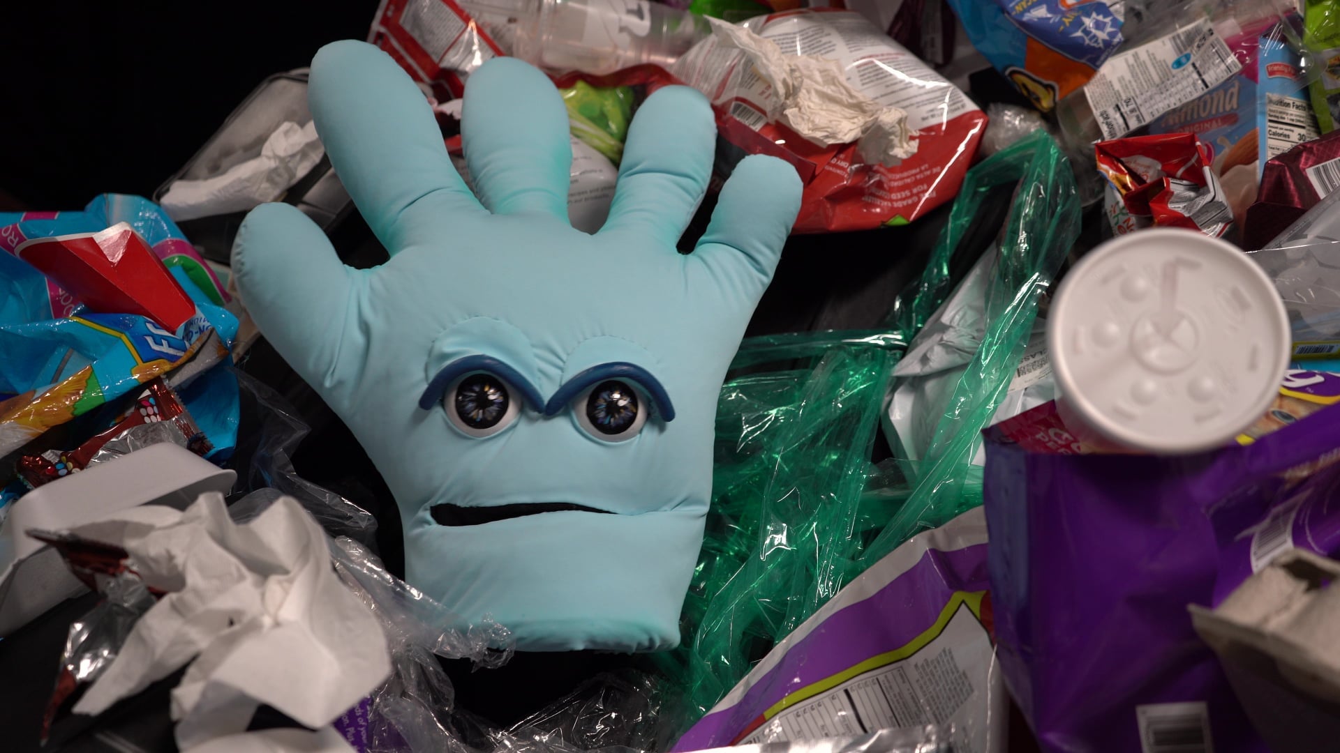 A plastic glove with eyes and a mouth sits amongst plastic trash