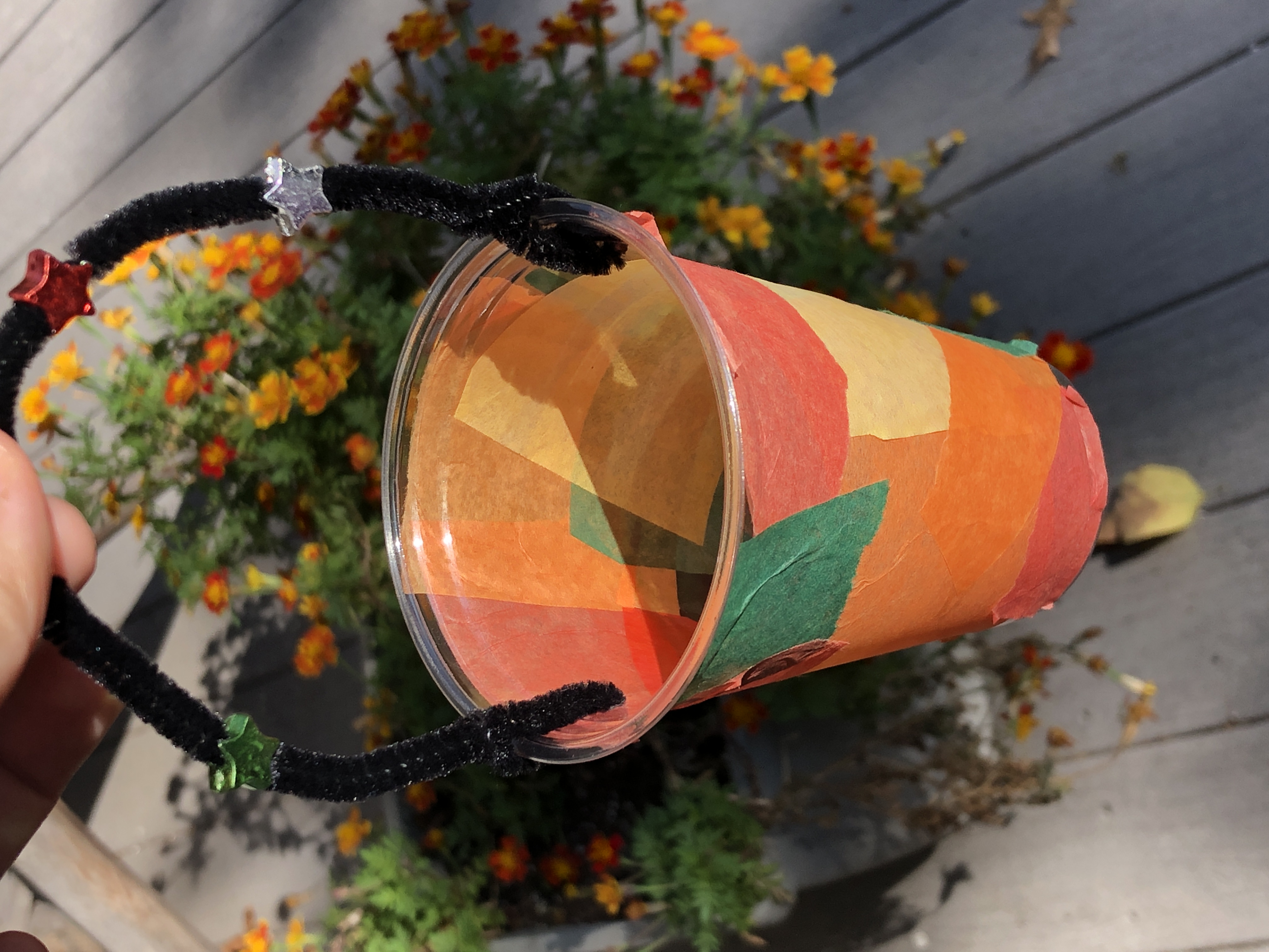 A DIY lantern is held up over a background of gold and orange flowers. 