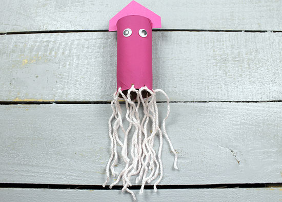 A pink squid made from a toilet paper roll, construction paper, string, and googly eyes. 