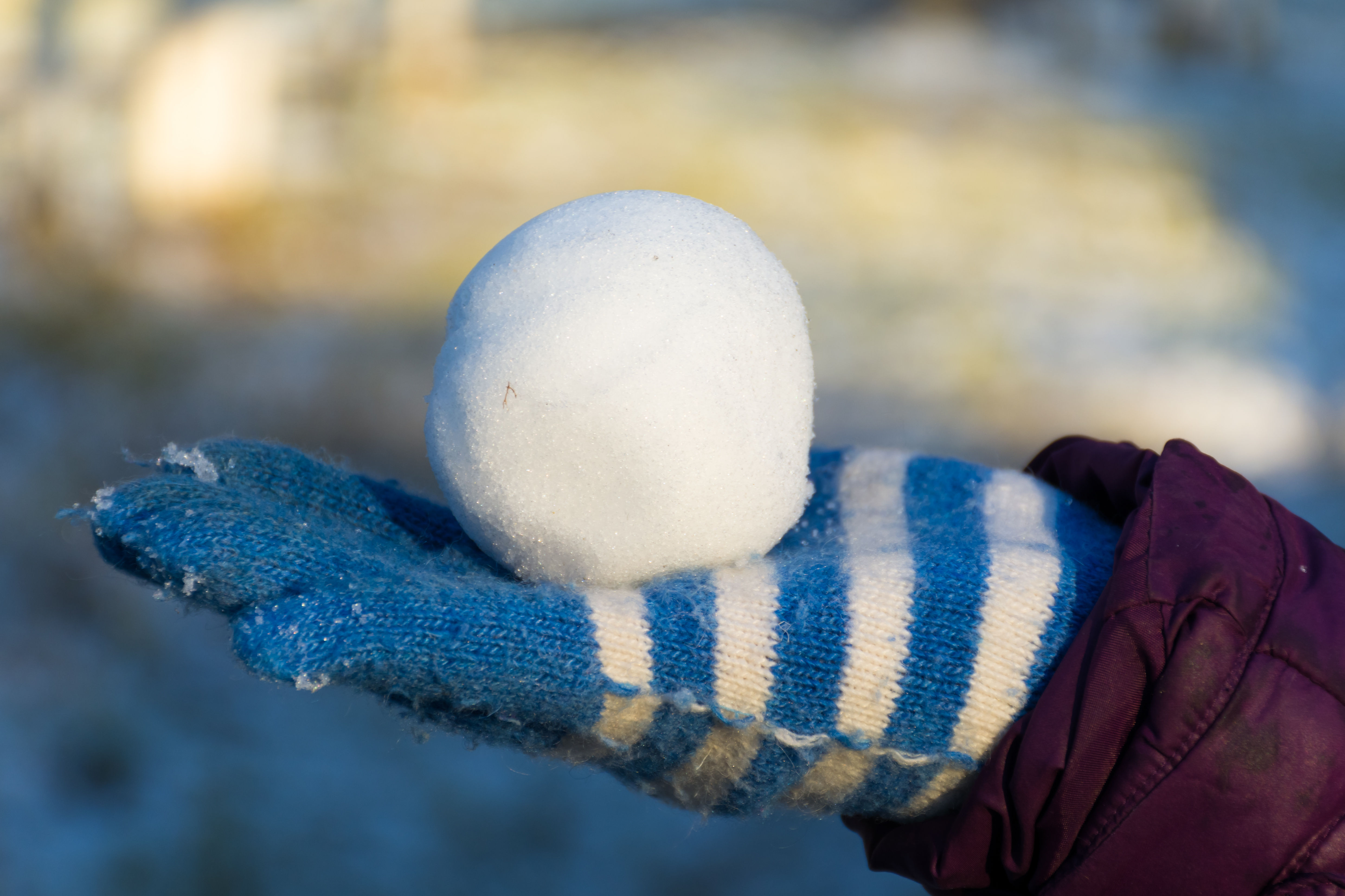 Snowball in a child's gloved hand. The glove is blue and white striped. 