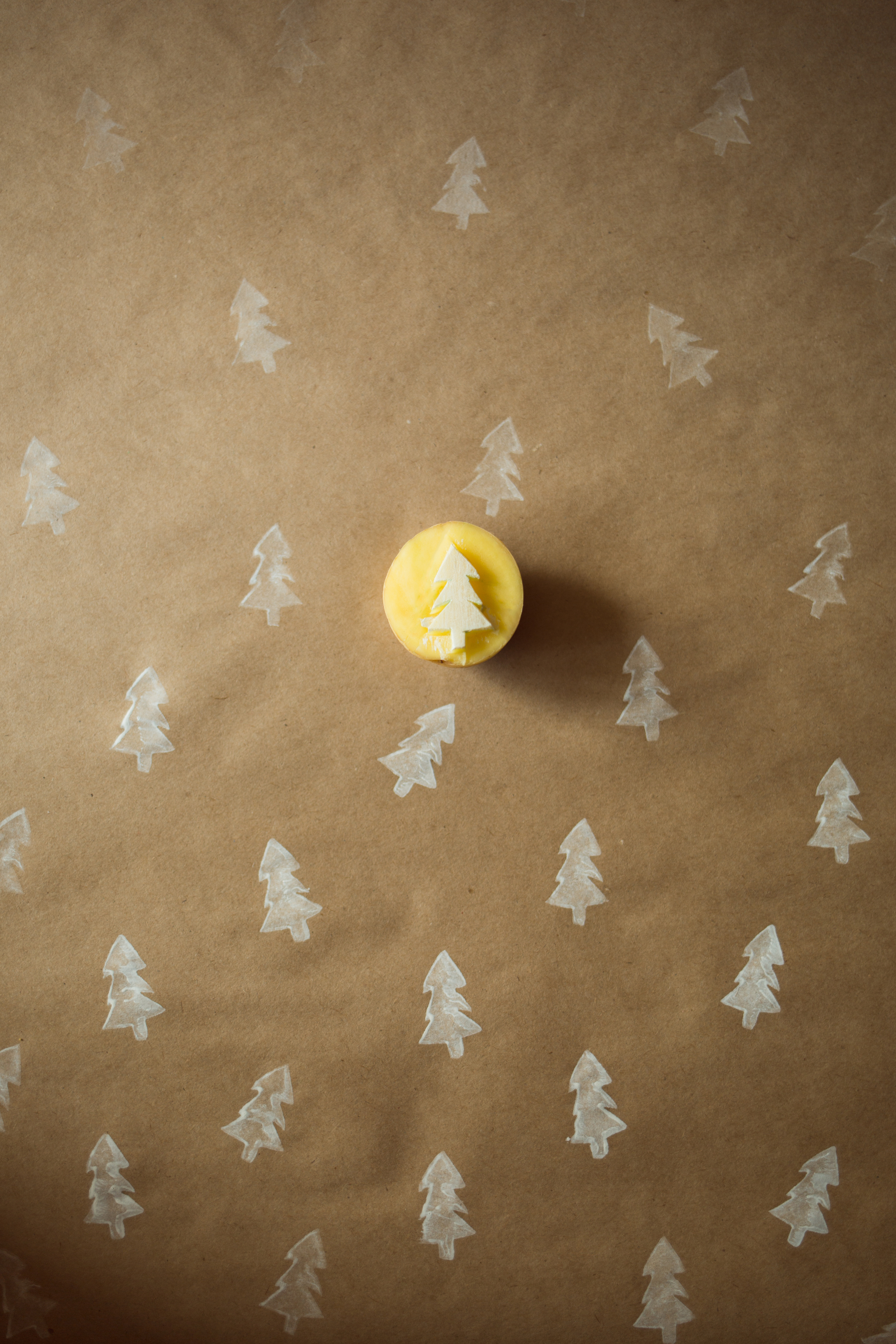 Brown kraft paper background with white pine trees stamped on top, featuring a carved potato with a pine tree. 