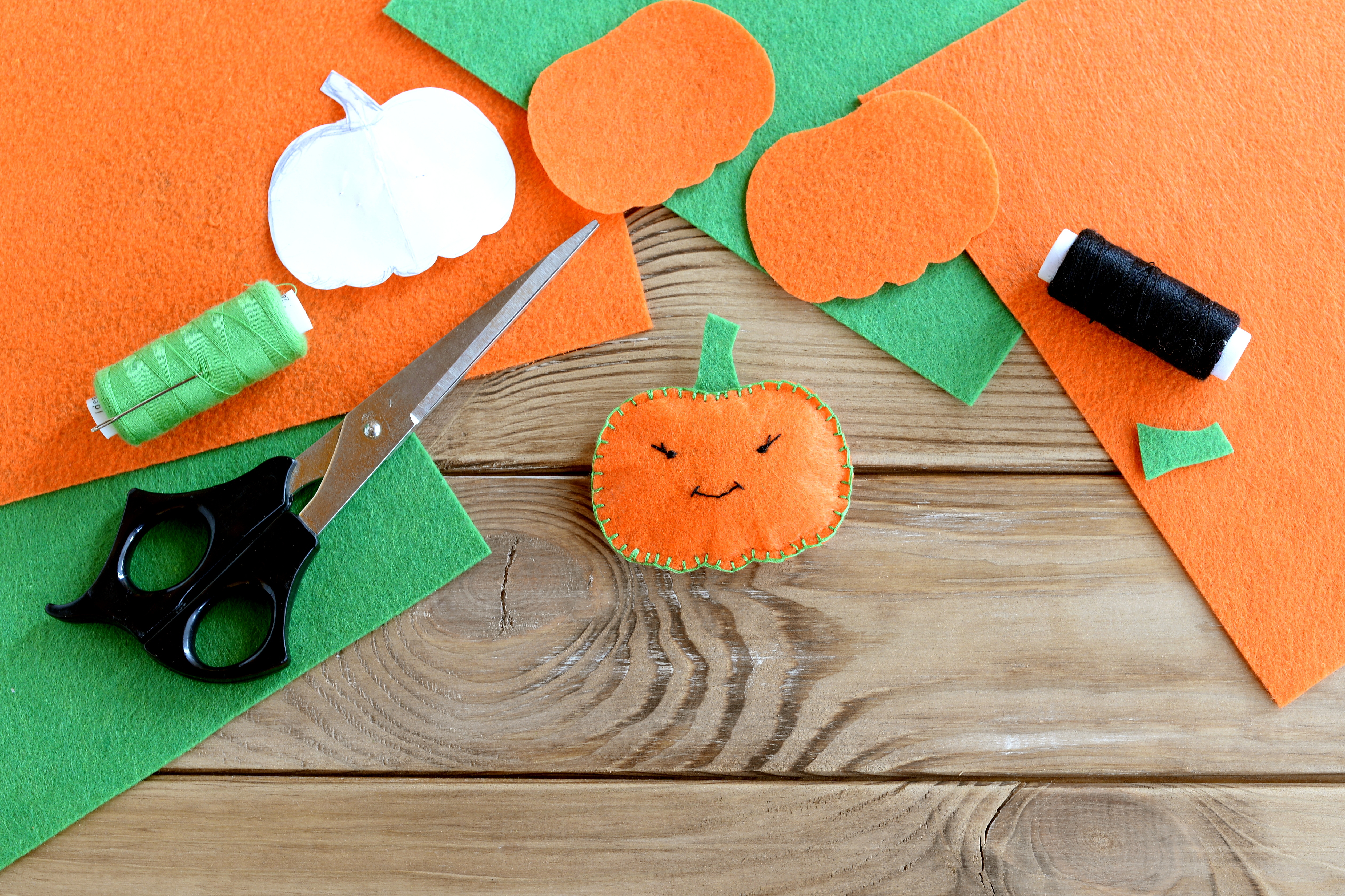 Artfully aranged orange and green felt with scissors, thread, and a finished sewn felt pumpkin.