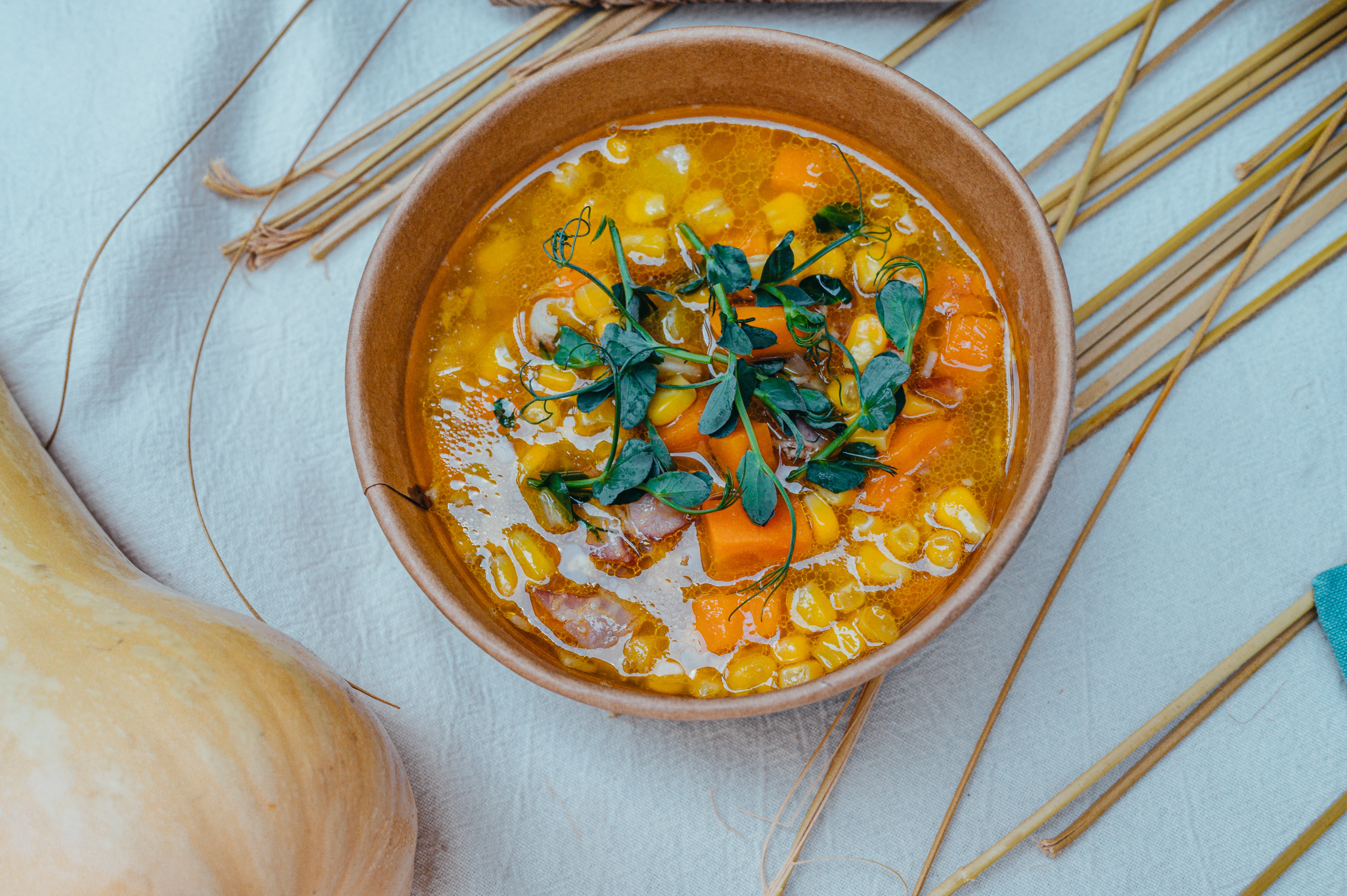A bowl of yummy brothy soup with a variety of yellow and orange vegetables topped with cilantro. 