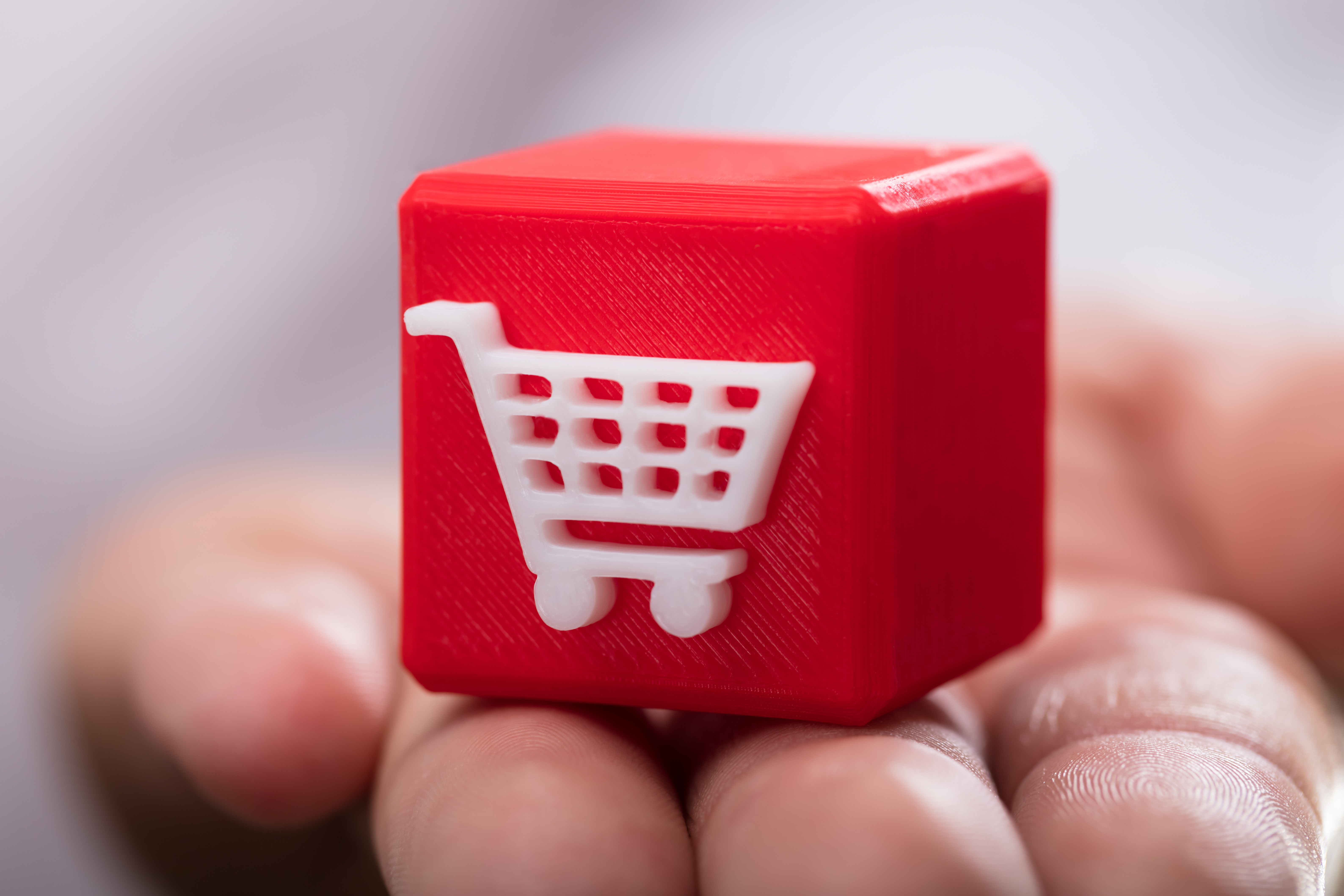 a hand holding a red cube with a white shopping cart