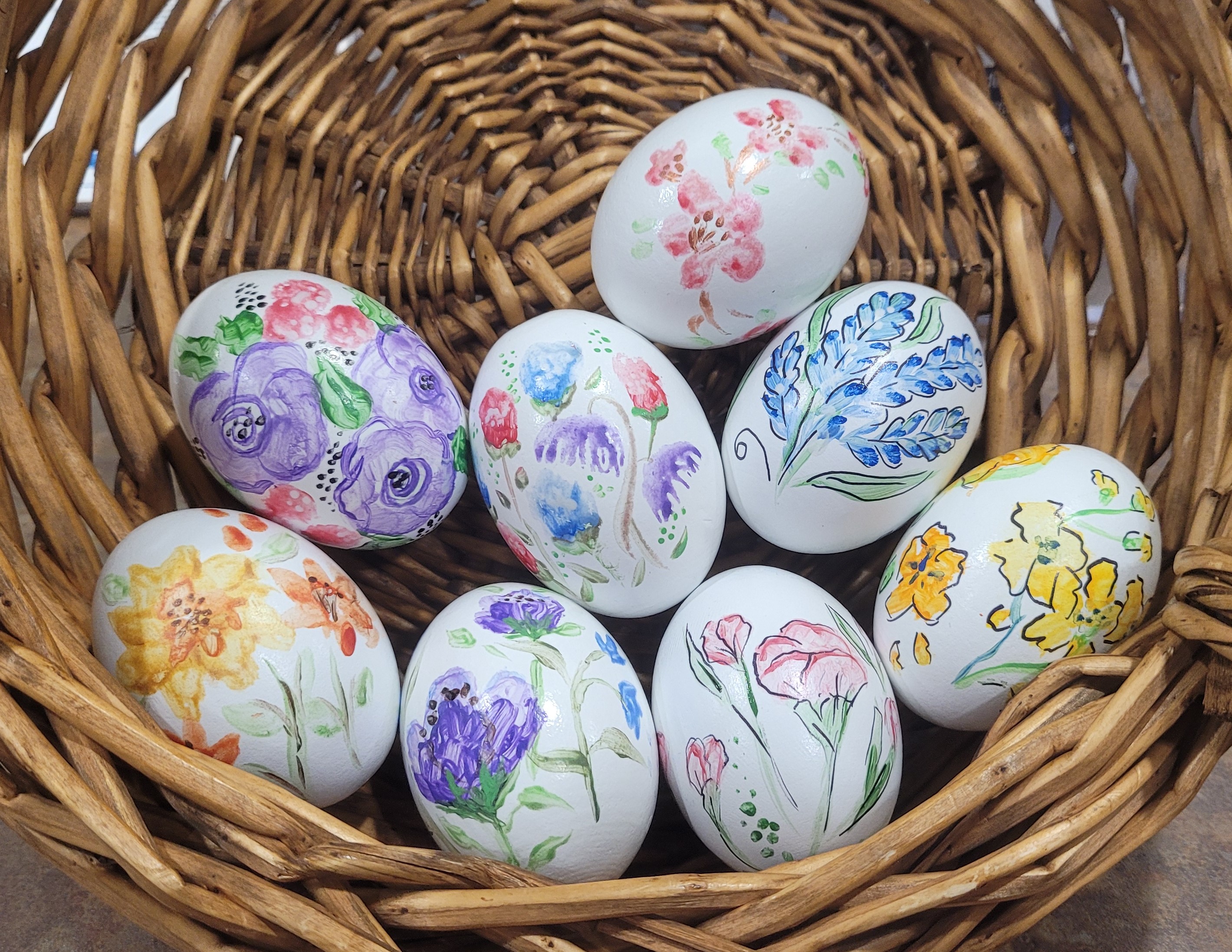 White eggs painted with pastel flowers in a basket.