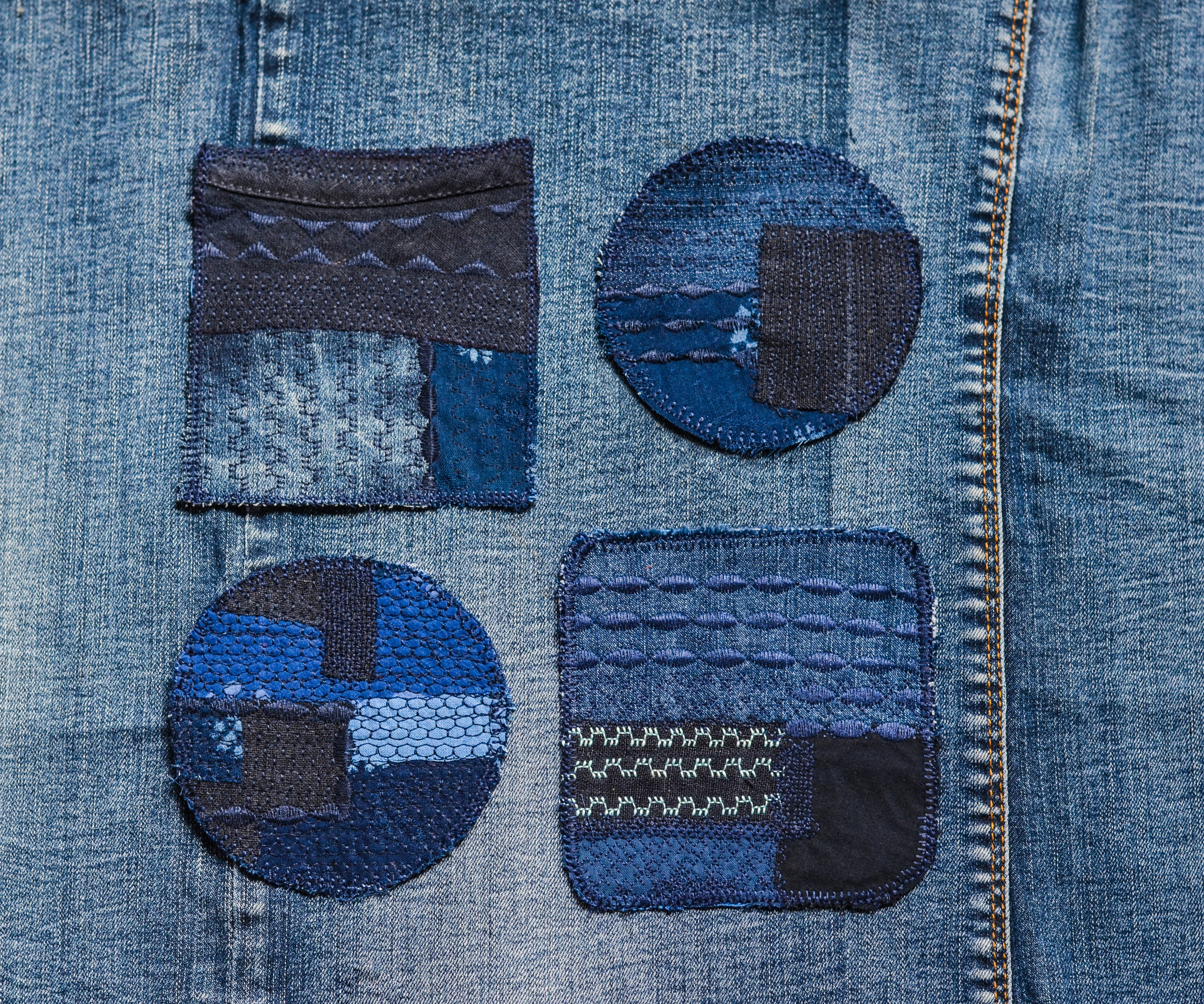 A denim piece of fabric with four visible mending patches sewn on it. 