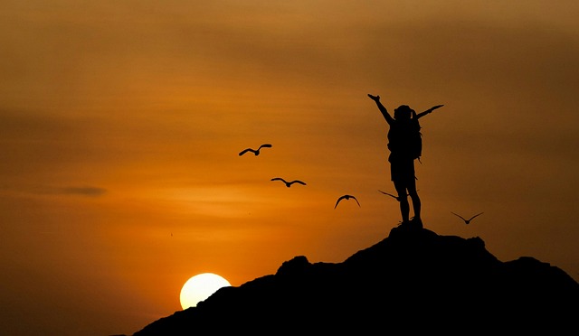 A person raising their hands on a hill, watching the sunset. 