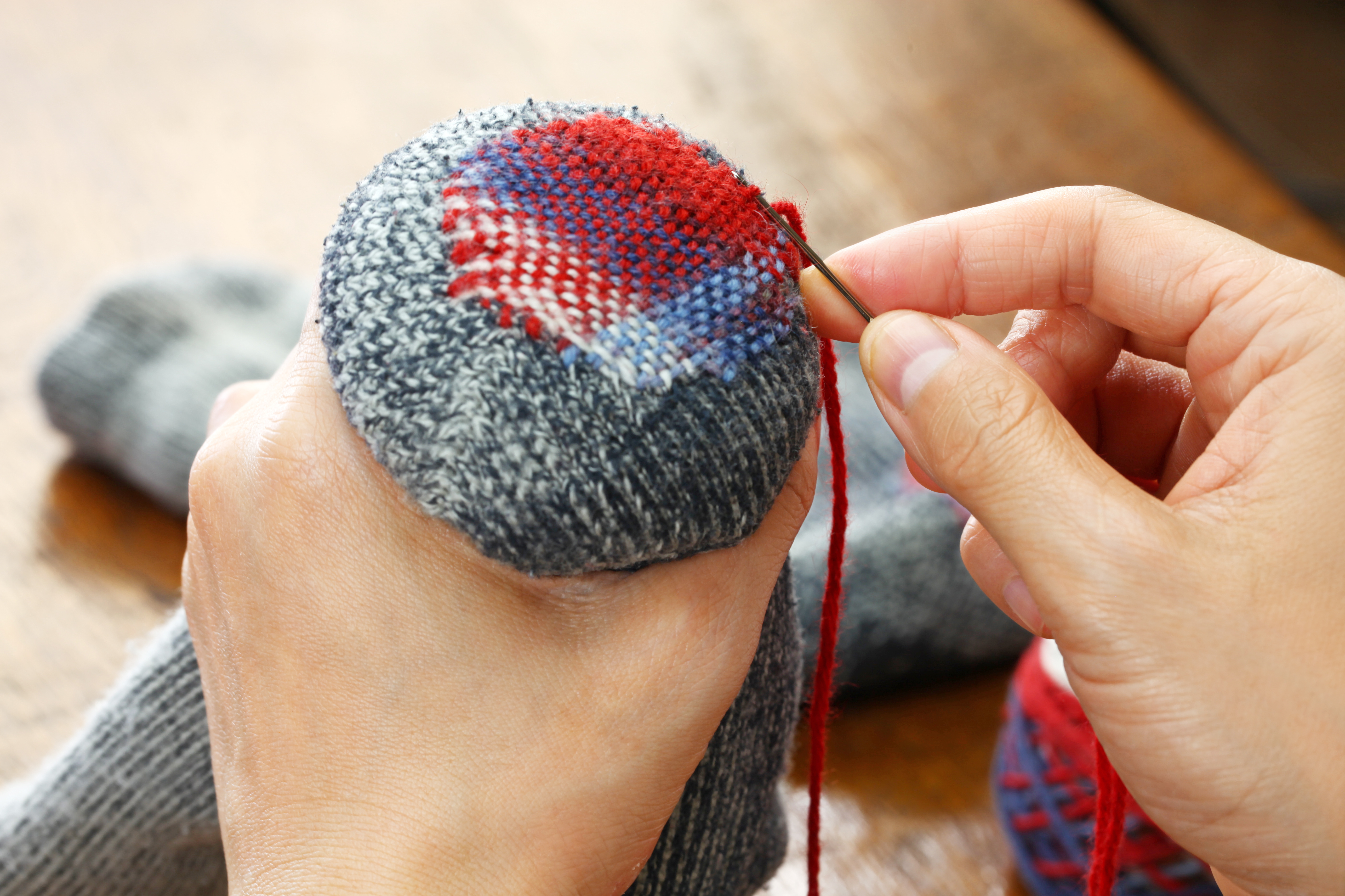 A pair of hands mending a sock through colorful darning.