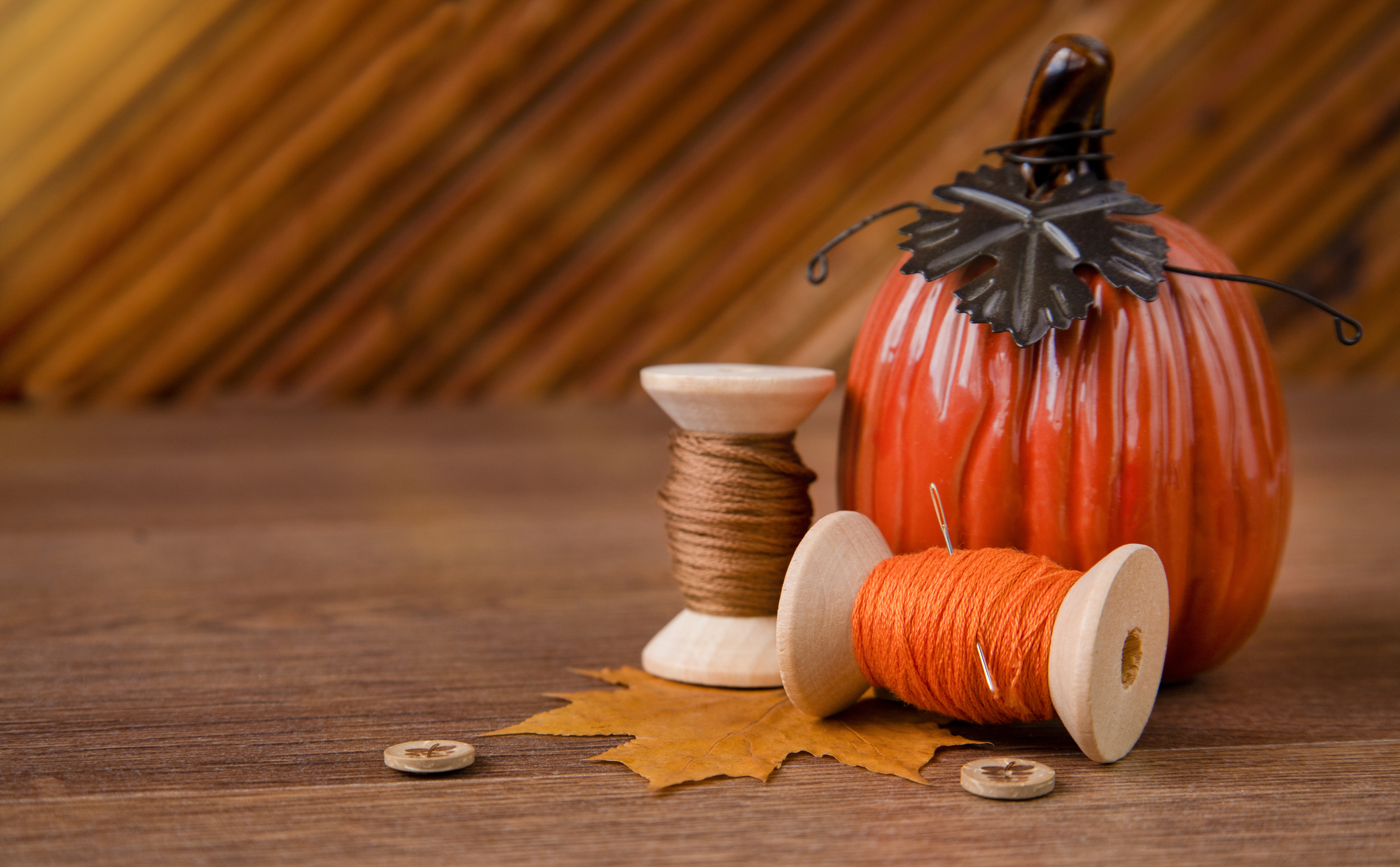 An aesthetic arrangement of a ceramic pumpkin with wooden spools of fall colored thread.