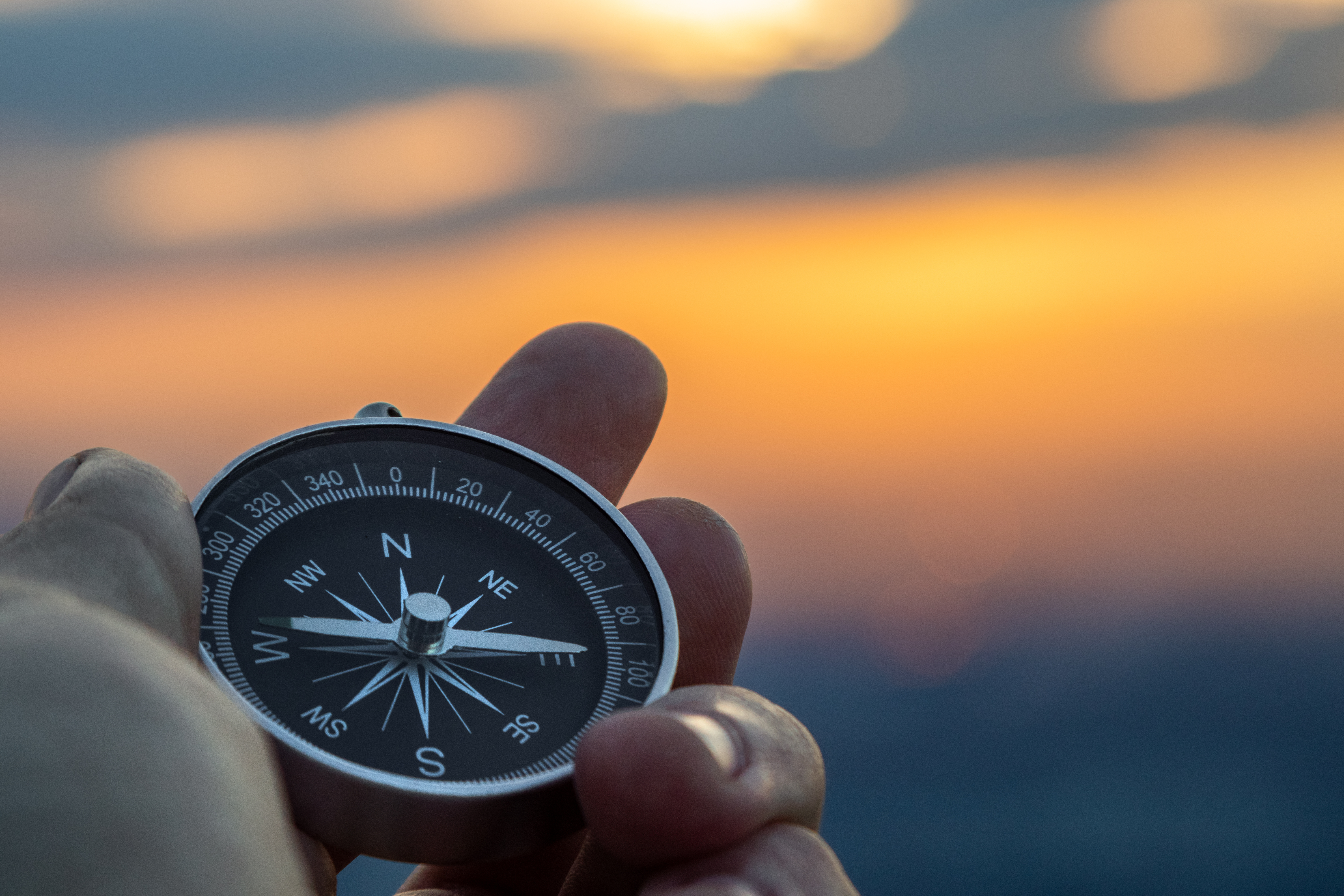 Hand is holding up a compass over a sunset 