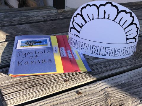 The Kansas Day symbols flipbook and crown sit on a picnic bench outside of the Schlagle library.