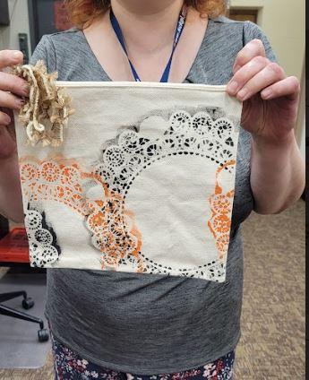 zippered canvas bag with doily patterns being held by staff member