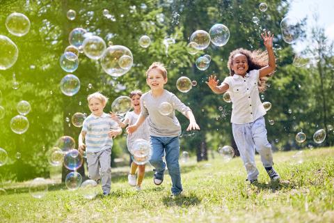 Children playing with bubbles in open grassy area.