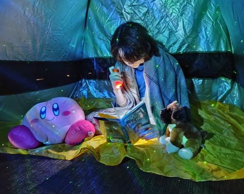 Student reading a book in a tent.