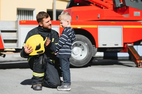 firefighter showing child his helmet in front of a fire truck