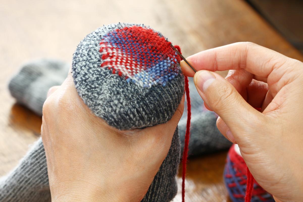 A pair of hands mending a sock through colorful darning.